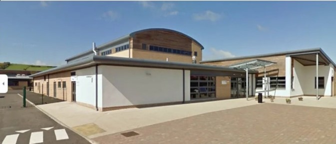 A school building with a curved roof. The building is tan and brown. A paved area is in front A school building with a curved roof. The building is tan and brown. A paved area is in front